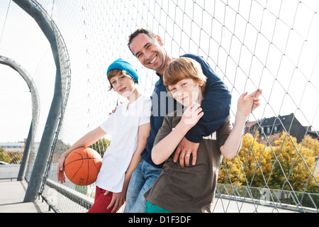 Padre e i due figli con basket sul campo sportivo Foto Stock