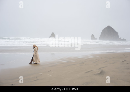 La donna parla al telefono con Haystack Rock in la distanza in una popolare destinazione turistica, Cannon Beach, Oregon, Stati Uniti d'America Foto Stock