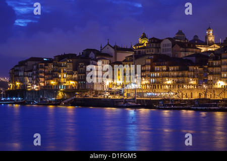 Città illuminata edifici e barche che riflette le luci colorate nel fiume Douro lungo il lungomare di Porto, Portogallo al crepuscolo Foto Stock