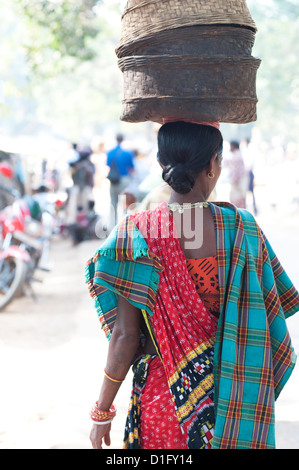 Donna al settimanale mercato tribale indossando vivacemente colorato abbigliamento e cestelli porta sulla sua testa, Bissam Cuttack, Orissa, India Foto Stock