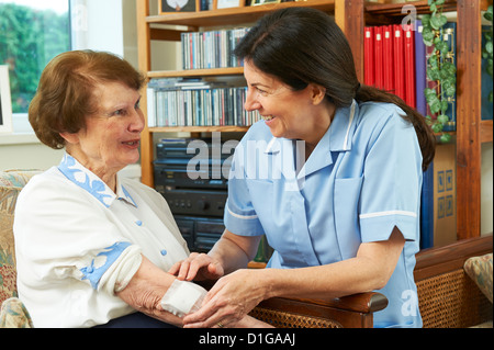 Lavoratore di cura di salute di medicazione sulla ferita un senior womans arm a casa Foto Stock