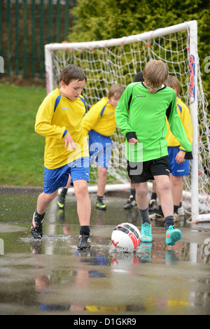 I ragazzi della scuola dribbling un calcio alla fine di un piovuto off pratica corrispondono a Nostra Signora & San Werburgh Cattolico della scuola primaria Foto Stock