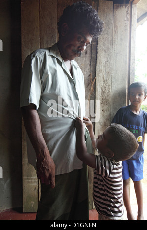 Galle, Sri Lanka, un bambino aiutando il suo padre disabili in abbottonatura suo shirt Foto Stock