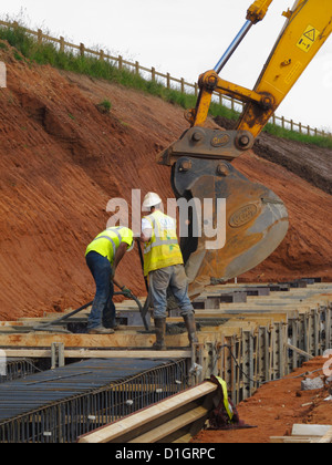 La colata di cemento da una benna di scavo per un cemento armato ponte striscia fondazione basamento vibro compattazione poker UK Foto Stock