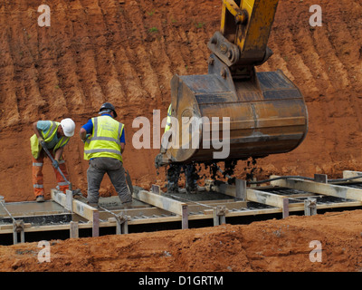 La colata di cemento da una benna di scavo per un cemento armato ponte striscia fondazione basamento vibro compattazione poker UK Foto Stock