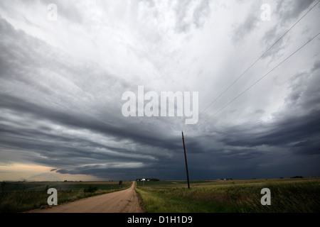 Un potente tempesta costituisce al di sopra di una strada di campagna, mentre un centro di irrigazione a perno spray di sistema sul lato. Foto Stock