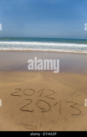 2012 e 2013 scritto nella sabbia sulla spiaggia con le onde del mare partendo per cancellare la parola Foto Stock