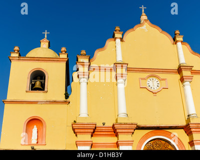 Sole sulla facciata gialla della chiesa cattolica con la torre campanaria e orologio Foto Stock