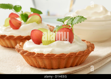 Piccole torte di crema e rabboccato con uve fresche Foto Stock