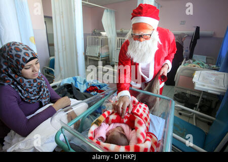 Dic. 23, 2012 - Ramallah, West Bank - palestinesi uomo vestito da Santa Claus fornisce ai bambini un presente in ospedale in Cisgiordania città di Ramallah. Palestinesi cristiani attraverso il popolo israeliano Palestinese occupata Cisgiordania si stanno preparando per le imminenti feste di Natale (credito Immagine: © Issam Rimawi APA/images/ZUMAPRESS.com) Foto Stock