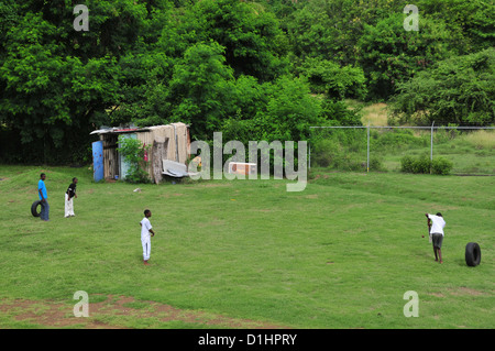 Quattro West Indian ragazzi giocare a cricket in abiti casual su erba, progressi Park Cricket Ground, Grenville, Grenada, West Indies Foto Stock