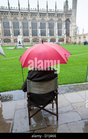 Kings College di Cambridge Regno Unito 24 dicembre 2012. Coda di folle in pioggia per i biglietti per il Festival di nove lezioni e canti natalizi svoltasi nella famosa cappella alla vigilia di Natale. Alcune persone si accamparono durante la notte e altri sono arrivati a 4.30am per assicurarsi un posto nella coda. Il concerto è trasmesso in tutto il mondo. Il meteo non hanno scoraggiato la gente gli spiriti. Foto Stock