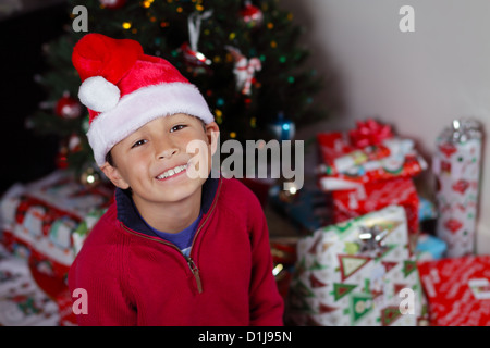 Ragazzo con Santa Hat nella parte anteriore di albero di Natale con luci e decorazioni - con spazio copia a destra Foto Stock