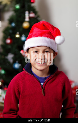 Ragazzo con Santa Hat nella parte anteriore di albero di Natale con luci e decorazioni Foto Stock