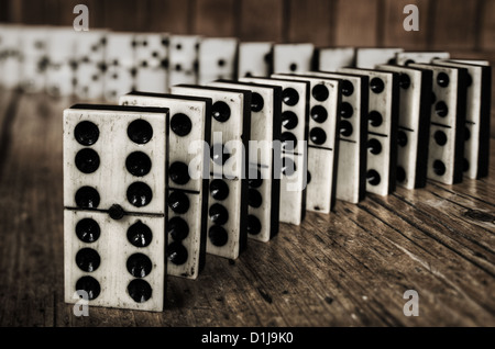 Righe di schierate vecchio avorio e ebano riposte in bronzo in piedi i blocchi di domino su pezzi di pino vittoriano tabella pannello di legno dietro Foto Stock