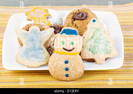 Pupazzo di neve cookie si erge davanti assortiti di vacanza i cookie su giallo tovaglia Foto Stock