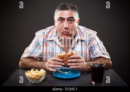 Ritratto di un uomo avido di mangiare hamburger su sfondo grigio Foto Stock