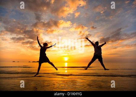 Coppia giovane in un salto sul mare spiaggia al tramonto Foto Stock