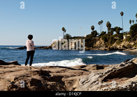 Asian lady in piedi sulle rocce al Laguna Beach in California per godersi il sole e il surf con palme lungo le cime della scogliera Foto Stock