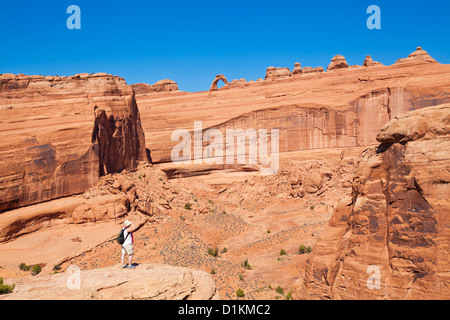 Turista femminile guardando verso Delicate Arch da nel Parco Nazionale di Arches nei pressi di Moab Utah USA Stati Uniti d'America Foto Stock
