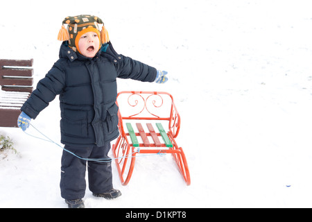 Piccolo ragazzo giocando con una slitta o lo slittino in snow ridendo come ama se stesso tirandola lungo Foto Stock