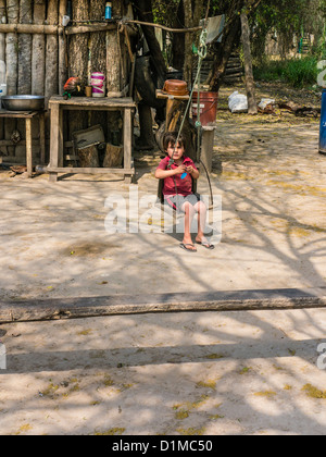 Giovane ragazzo su una oscillazione al di fuori del suo alloggiamento primitivo lungo l'autostrada nove nel Chaco Paraguay settentrionale. Foto Stock