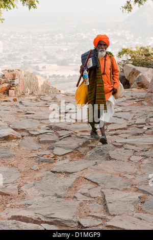 Un Sadhu (Hindu uomo santo) camminando su un sentiero acciottolato nella sua tunica arancione e turbante vicino a Pushkar Rajasthan in India Foto Stock