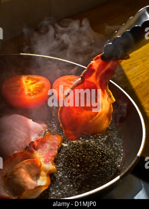 BACON RASHER PADELLA albero del sole illumina un rasher di organico back bacon essendo ruotata in una padella calda contenente pomodori Foto Stock