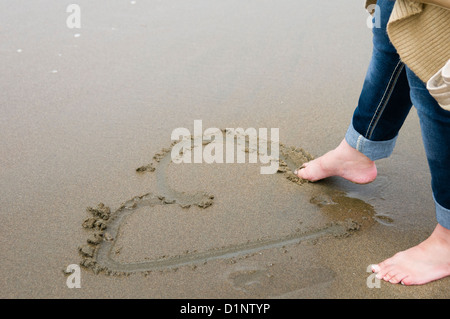 Donna di disegno di un cuore nella sabbia con le sue dita. Ocean Beach, San Francisco, California Foto Stock