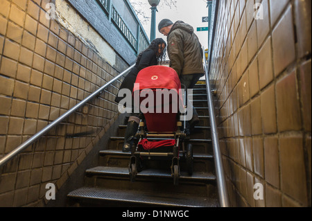 Una coppia porta un passeggino su per le scale fino all'uscita dalla metropolitana nel quartiere di Chelsea di New York Foto Stock