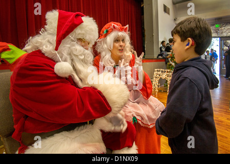 Un sordo ispanico boy comunica con un sordo Santa Claus e la sig.ra Santa utilizzando il linguaggio dei segni durante le feste di Natale Foto Stock