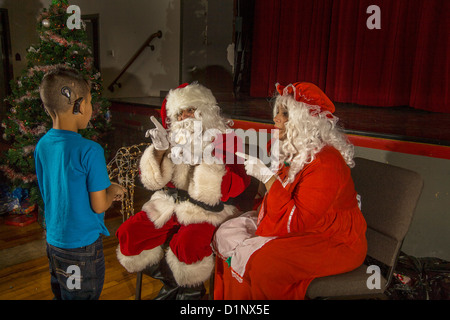 Sordi African American boy comunica con un sordo Santa Claus e la sig.ra Santa utilizzando il linguaggio dei segni durante le feste di Natale. Foto Stock