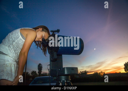 Al tramonto un otto-anno-vecchia ragazza guarda attraverso l'oculare di un catadiottrico telescopio astronomico nel suo cortile della California. Foto Stock