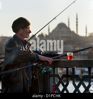 Uomo di pesca in un fiume con Rustem Pasha moschea in background, Fiume sul Bosforo, Istanbul, Turchia Foto Stock