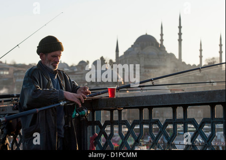 Uomo di pesca in un fiume con Rustem Pasha moschea in background, Fiume sul Bosforo, Istanbul, Turchia Foto Stock