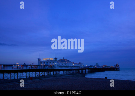 Il piacere di Brighton Pier al tramonto con il giovane sat stagliano sulla spiaggia, Brighton East Sussex, Inghilterra Foto Stock