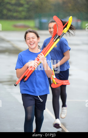 Le ragazze della scuola rush all'interno dalla pioggia che trasportano bastoni da hockey a Nostra Signora & San Werburgh Cattolico della scuola primaria a Newcastle- Foto Stock