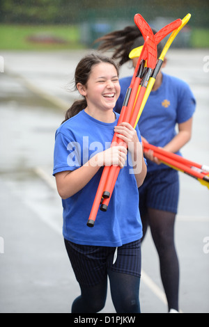Le ragazze della scuola rush all'interno dalla pioggia che trasportano bastoni da hockey a Nostra Signora & San Werburgh Cattolico della scuola primaria a Newcastle- Foto Stock