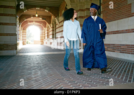 Figlia camminare con il padre nel tappo di graduazione e vestaglia Foto Stock