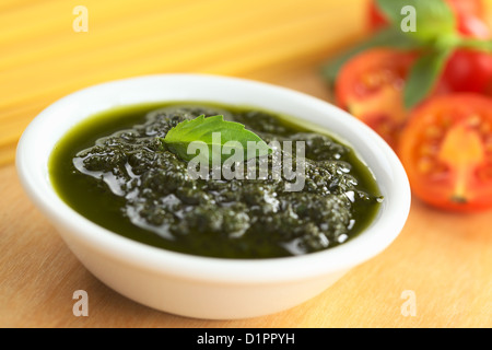 Pesto fresco fatto di basilico, aglio e olio di oliva in una piccola ciotola e guarnito con una foglia di basilico Foto Stock