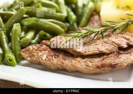 Carni bovine fette di carne con rosmarino fresco sulla parte superiore, servita con fagiolini e patate cotte Foto Stock