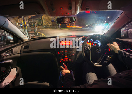Un autista in attesa per le spie verde per attivare la notte dall'interno dell'auto. Foto Stock