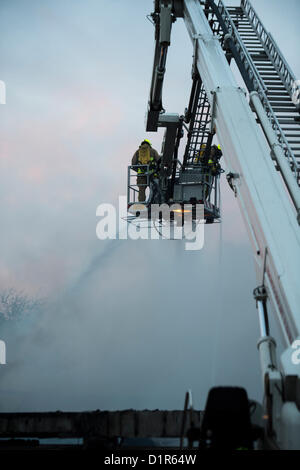 Laindon, Basildon, Essex. Quattro negozi sono stati rasi al suolo dopo un incendio appiccato in un cinese take-away in parata noto come il Triangolo negozi. Si ritiene che l incendio è scoppiato in un aeratore e diffondersi a tutta la sfilata di distruggere altre tre imprese. Gli altri negozi erano un parrucchiere, un ufficio postale e un negozio di generi alimentari. Non è noto per aver causato danni. Due vigili del fuoco su di una piattaforma aerea la spruzzatura del tetto. Foto Stock