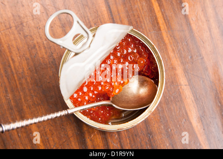 Caviale rosso in banca con il cucchiaio su uno sfondo di legno Foto Stock