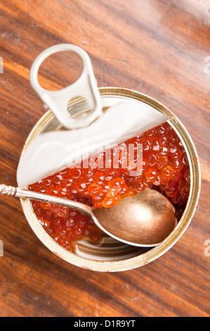 Caviale rosso in banca con il cucchiaio su uno sfondo di legno Foto Stock