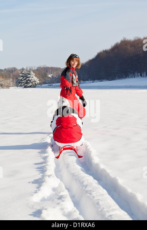 Donna di mezza età rosso di trazione slitta con sua figlia in un campo di neve Foto Stock