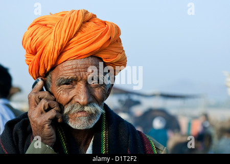 Una foto di un cammello commerciante in un turban arancione a Pushkar camel fair in Rajasthan in India a parlare su un telefono mobile Foto Stock