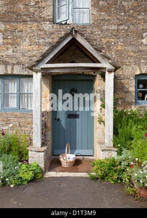 Pretty Cotswold cottage porta con cestello e fiori Foto Stock