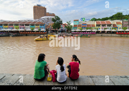 Tre donne seduti sul Fiume Singapore bank si affaccia sul dipinto luminosamente intrattenimenti di Clarke Quay Foto Stock