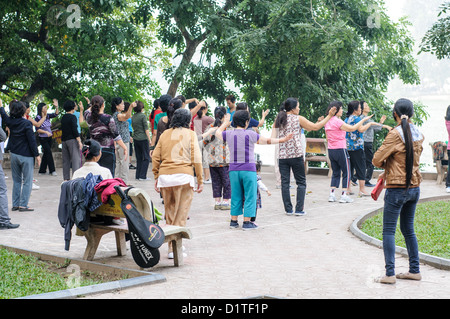 HANOI, Vietnam - le donne locali praticano il Tai chi durante la loro routine mattutina lungo le rive del lago Hoan Kiem nel centro di Hanoi. L'incontro quotidiano rappresenta un aspetto tradizionale della cultura urbana vietnamita, combinando l'esercizio fisico con l'interazione sociale. Il lago è un luogo popolare per le attività della comunità nel cuore del centro storico della città. Foto Stock